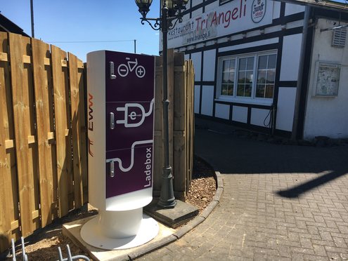 Pedelecbox Öffentliche Ladesäule für E-Bikes auf einem Gehweg vor einem Gebäude.