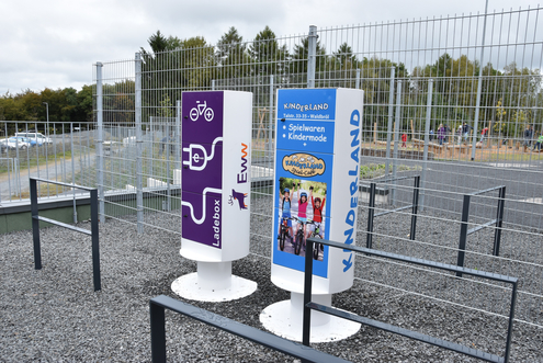 Pedelecbox_Panarbora Zwei öffentliche Ladesäulen für E-Bikes und Elektrofahrzeuge auf einem eingezäunten Gelände.
