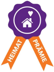 Waldbröl - Startseite (3) Lila Abzeichen mit Haus- und Herzsymbol sowie orangefarbenen Bändern mit der Aufschrift „Heimat Prämie“.